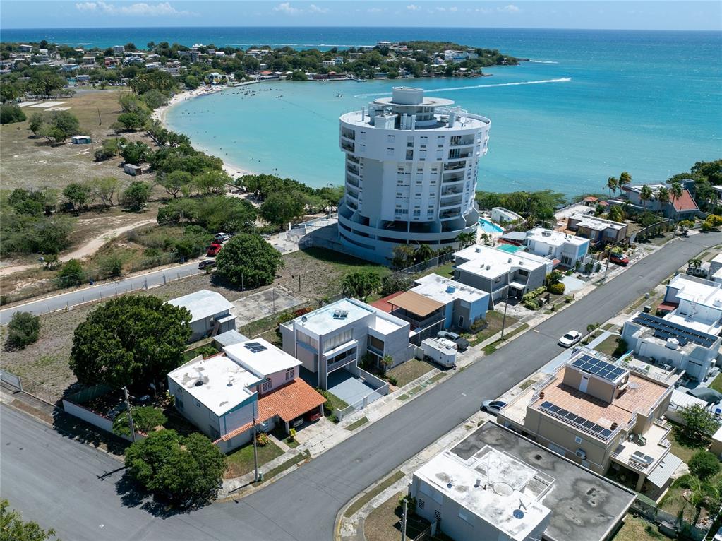An aerial view shows a circular high-rise building situated on a beach near residential houses — Playa Santa CALLE 3 UNIT D-13, ENSENADA, PR