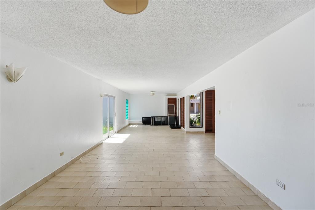 An empty, white-walled room features light-colored tile flooring, a sliding glass door, and recessed lighting — Playa Santa CALLE 3 UNIT D-13, ENSENADA, PR