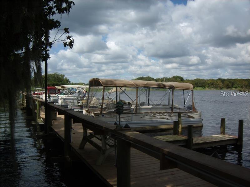 A wooden dock extends into a lake with several pontoon boats moored alongside it — 205 SHER LANE, DEBARY, FL