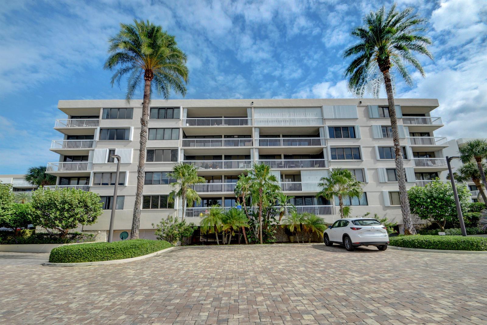 A multi-story apartment building with balconies and palm trees stands behind a paved parking area — 3250 S Ocean Boulevard # 207s, Palm Beach FL 33480, PALM BEACH, FL