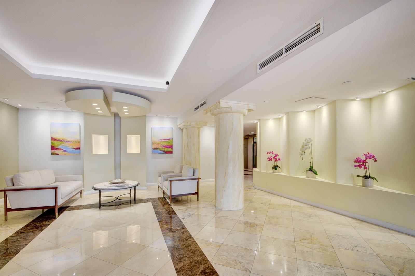 A bright lobby features marble floors, decorative columns, white seating, and recessed wall niches with flowers — 3250 S Ocean Boulevard # 207s, Palm Beach FL 33480, PALM BEACH, FL