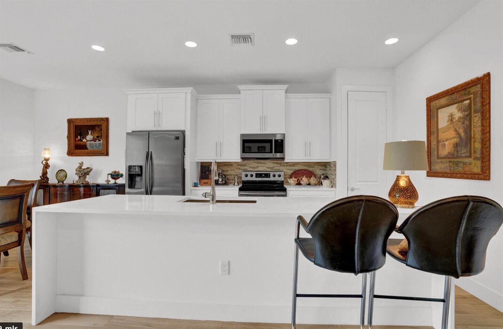 A modern kitchen features white cabinetry, a large waterfall island, and stainless steel appliances — 3199 Santa Catalina Place, FL 33467, FL