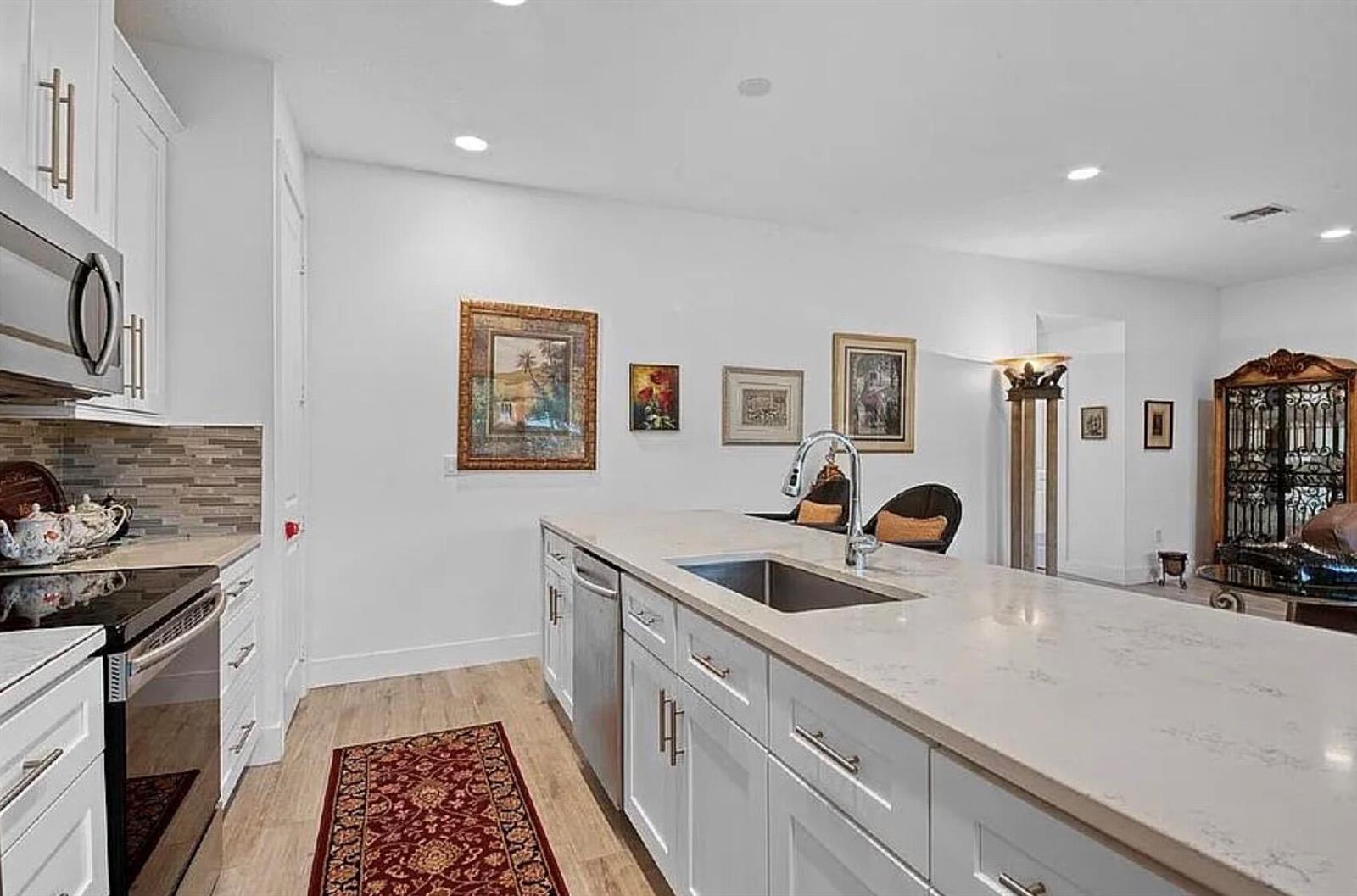 A kitchen features white cabinets, a large quartz island with a sink, and wood flooring — 3199 Santa Catalina Place, FL 33467, FL