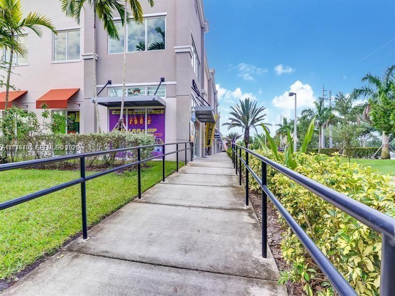 A concrete walkway with black metal railings leads toward a commercial building with storefronts — 2101 SW 101st Ave # 204, Miramar FL 33025, MIRAMAR, FL
