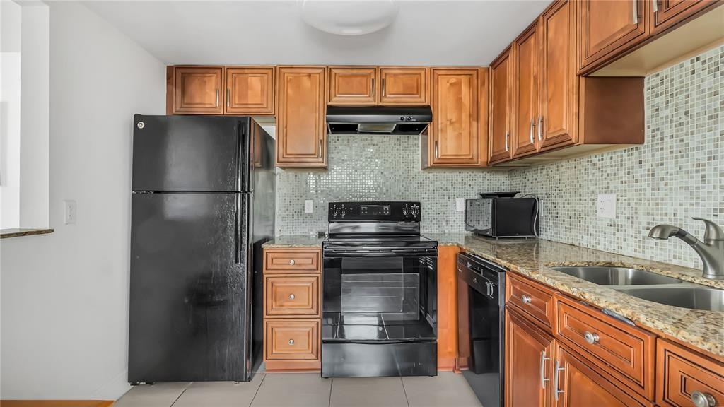 A kitchen with wood cabinets, black appliances, granite countertops, and a mosaic tile backsplash — 703 Brittany # O, Delray Beach FL 33446, DELRAY BEACH, FL