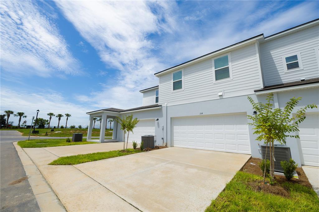 A two-story townhouse exterior with a white garage, light siding, and a concrete driveway — 104 ROYAL RANCH ROAD, GROVELAND, FL