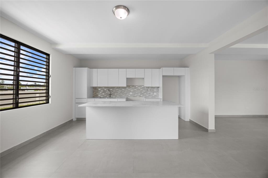 A modern kitchen features white cabinetry, a marble-topped island, and light gray tile flooring — 4 REXVILLE VAN SCOY, BAYAMON, PR