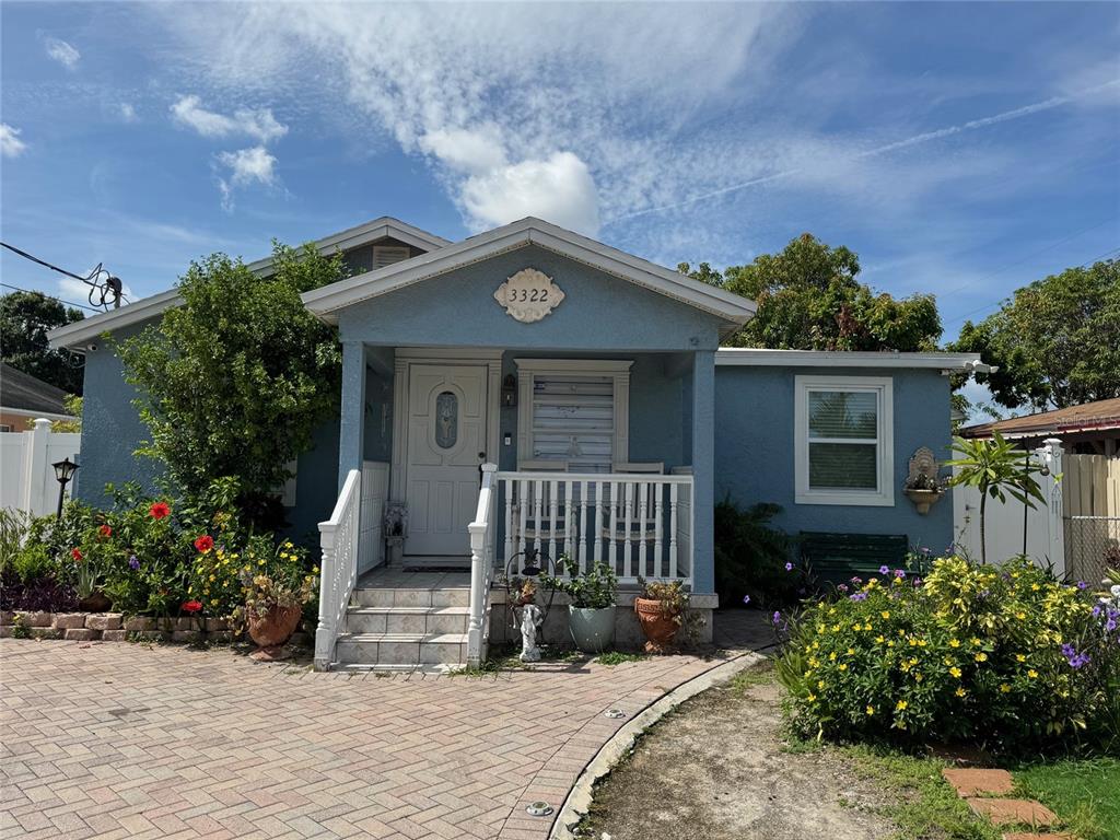 A blue single-story house features a front porch, a paved driveway, and landscaped garden beds — 3322 W SAINT JOSEPH STREET, TAMPA, FL