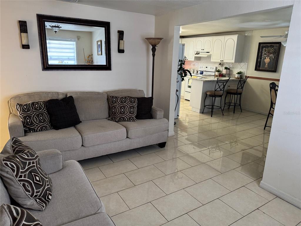 A living room with a light gray sofa opens into a kitchen with white cabinetry — 3322 W SAINT JOSEPH STREET, TAMPA, FL