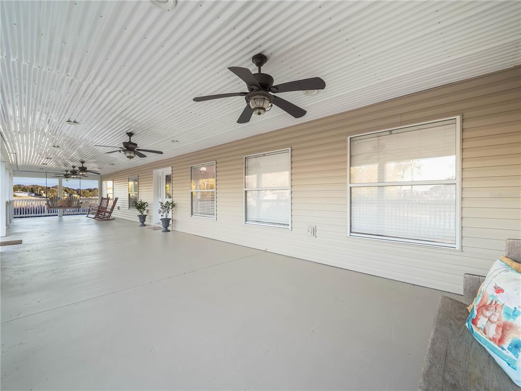 A long, covered porch features a gray concrete floor, ceiling fans, and beige siding — 124 PANGOLA DRIVE, WINTER HAVEN, FL