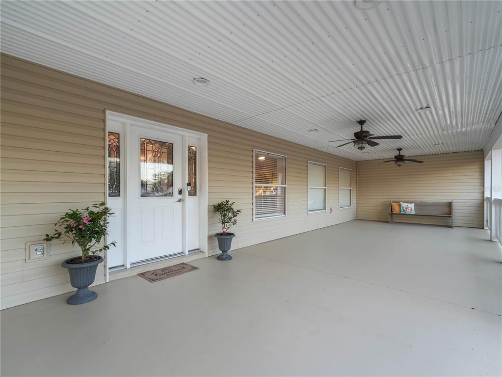 A wide, covered porch features beige siding, a white front door, and two ceiling fans — 124 PANGOLA DRIVE, WINTER HAVEN, FL