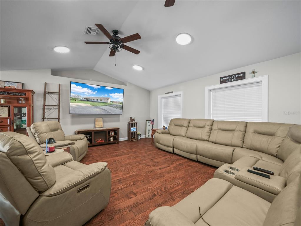 A living room features light-colored reclining furniture, wood-look flooring, and a wall-mounted television — 124 PANGOLA DRIVE, WINTER HAVEN, FL
