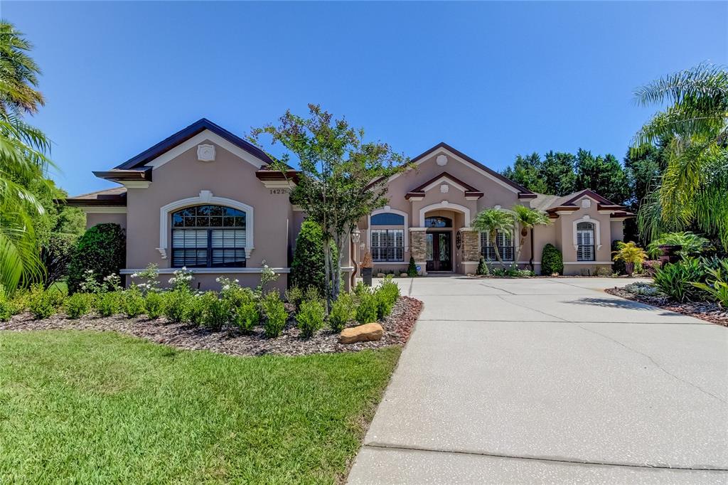 A single-story stucco house with a concrete driveway, arched windows, and lush landscaping — 1422 ARISTIDES COURT, ODESSA, FL