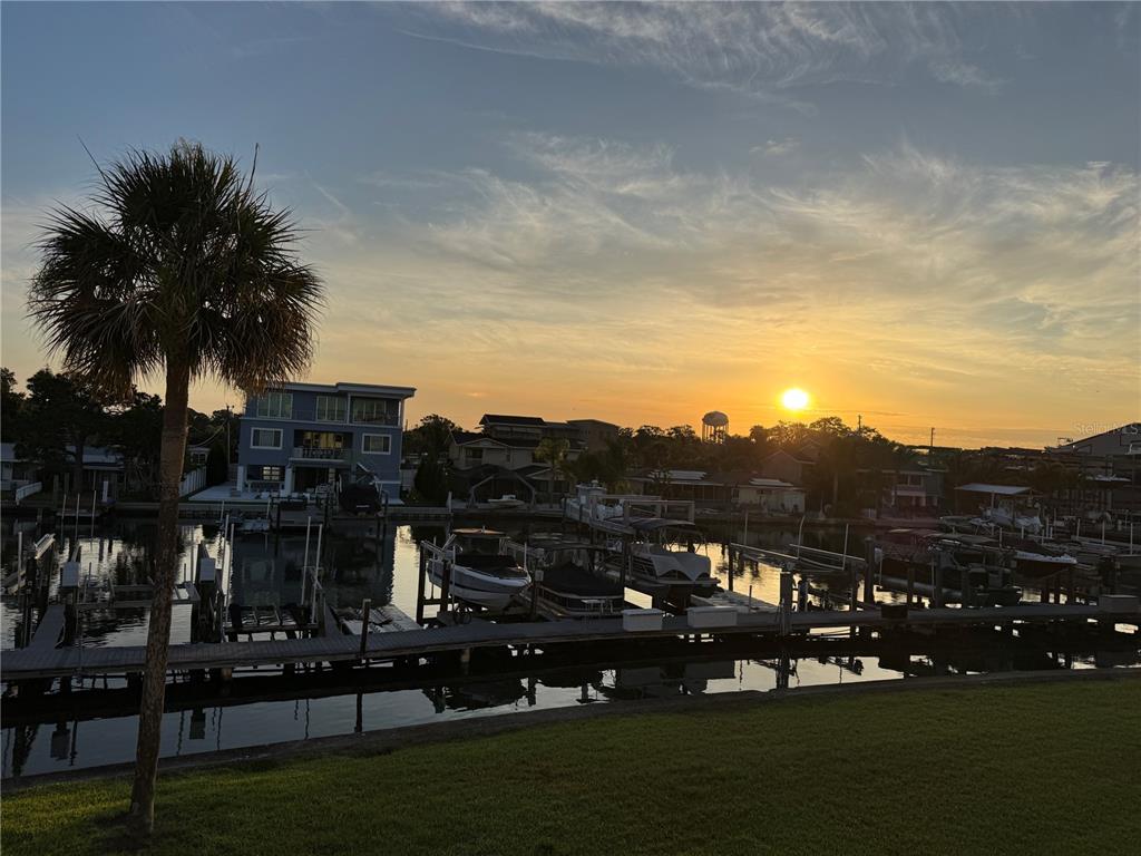 A sunset view over a canal with boat docks, a palm tree, and residential houses — 2395 HANOVER DR, DUNEDIN, FL