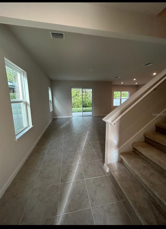 An open-concept living area with tile floors, a carpeted staircase, and sliding glass patio doors — 11931 THORNCREST DRIVE, SPRING HILL, FL