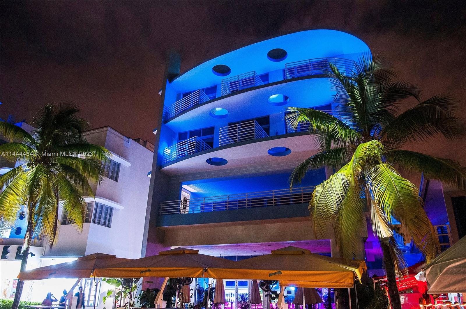 A multi-story building with blue exterior lighting and balconies stands at night beside palm trees — 1052 Ocean Dr # C503, Miami Beach FL 33139, MIAMI BEACH, FL