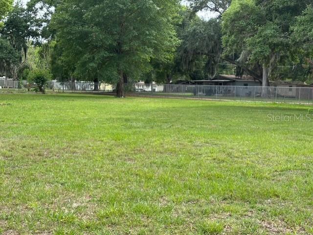 A grassy, vacant lot is enclosed by a chain-link fence with trees in the background — 3790 AVENUE U NW, WINTER HAVEN, FL