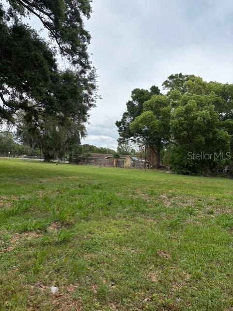 A grassy, open lot features mature trees and a distant house with a wooden fence — 3790 AVENUE U NW, WINTER HAVEN, FL