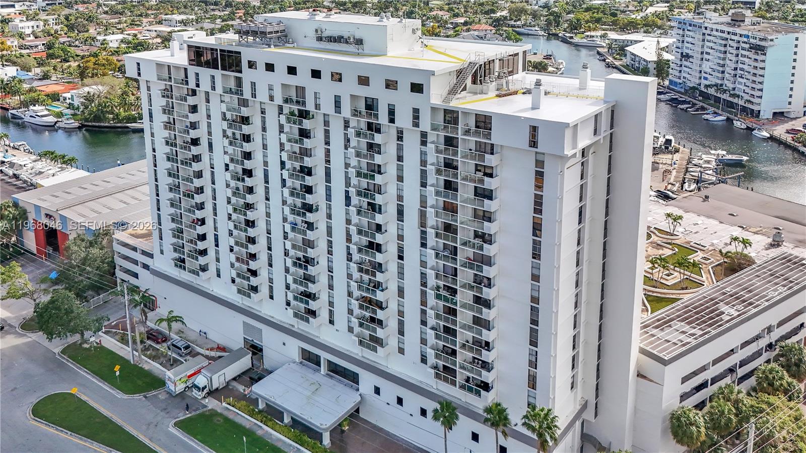 An aerial view of a tall white residential building with balconies next to a canal — 13499 Biscayne Blvd # 3, North Miami FL 33181, NORTH MIAMI, FL