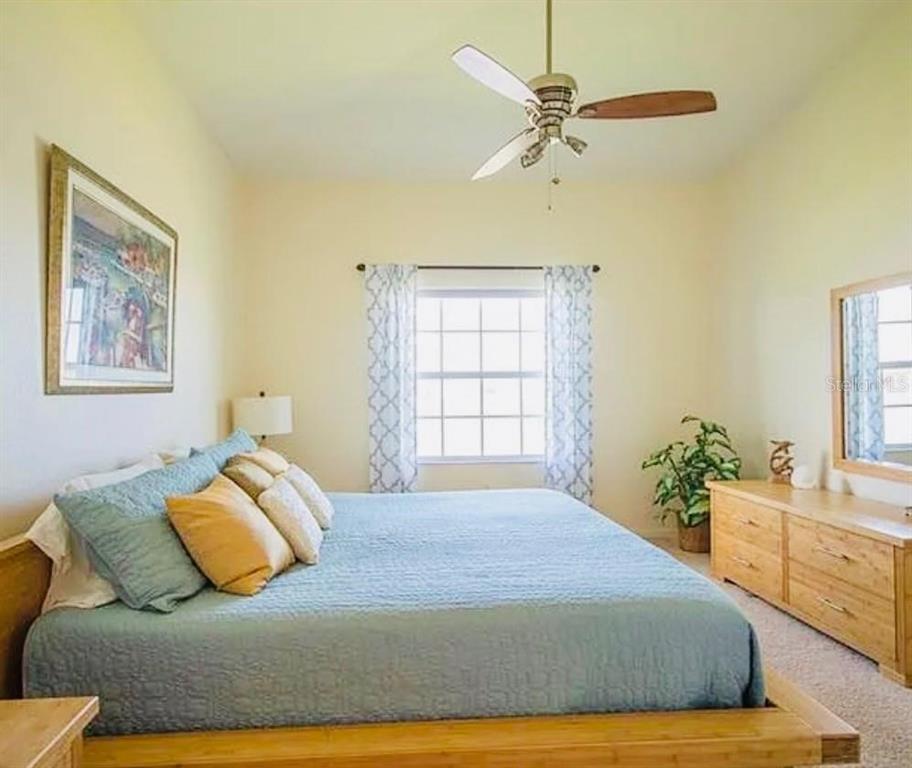 A bedroom features a bed with blue bedding, a wooden dresser, and a ceiling fan — 1457 SAN CRISTOBAL AVENUE UNIT 3203, PUNTA GORDA, FL
