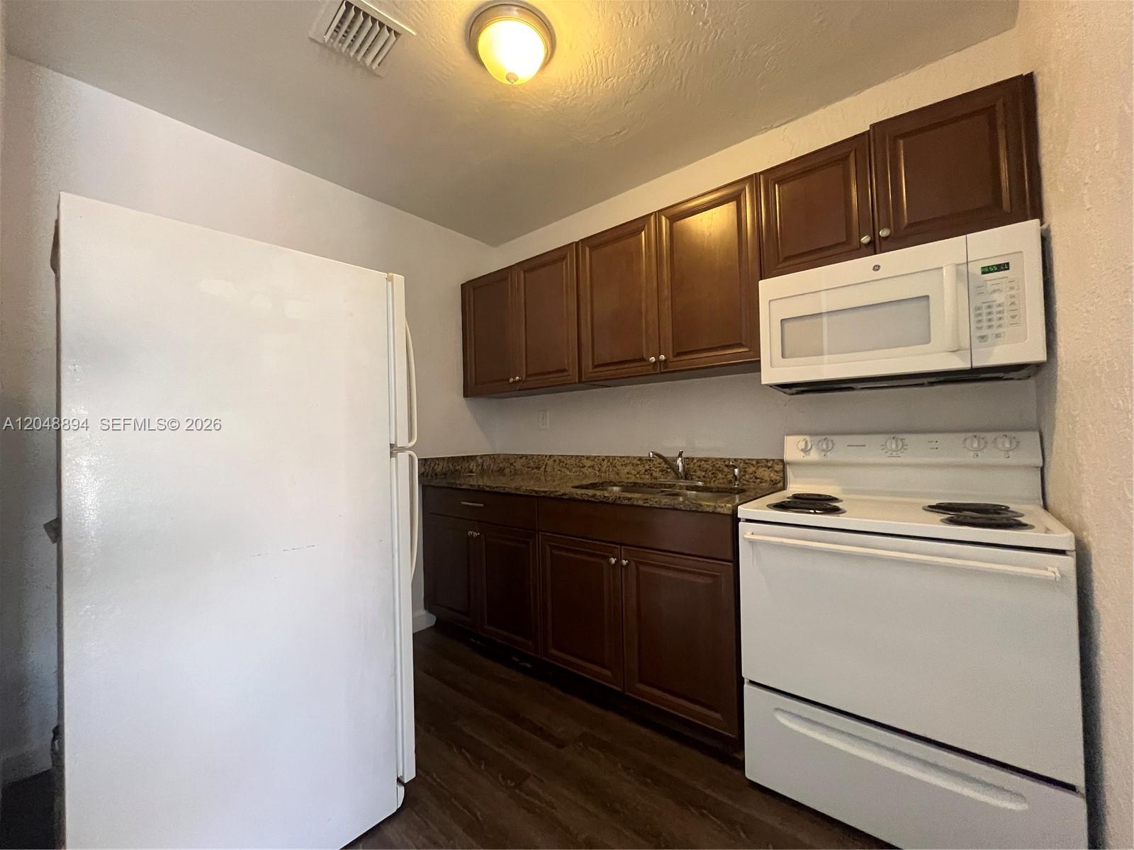 A kitchen features dark wood cabinets, granite countertops, and white appliances — 3024 NW 2nd St, Pompano Beach FL 33069, POMPANO BEACH, FL