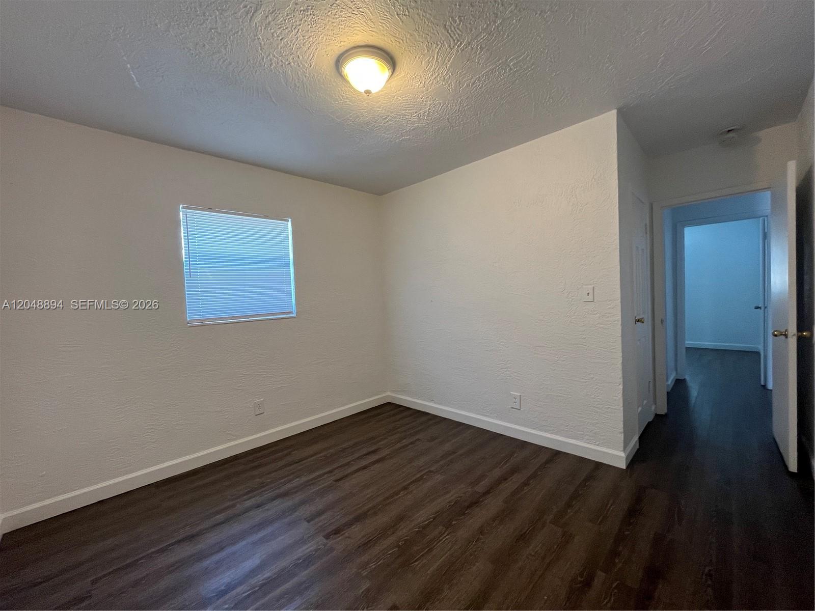 An empty bedroom features white textured walls, dark wood-look flooring, and a single ceiling light — 3024 NW 2nd St, Pompano Beach FL 33069, POMPANO BEACH, FL