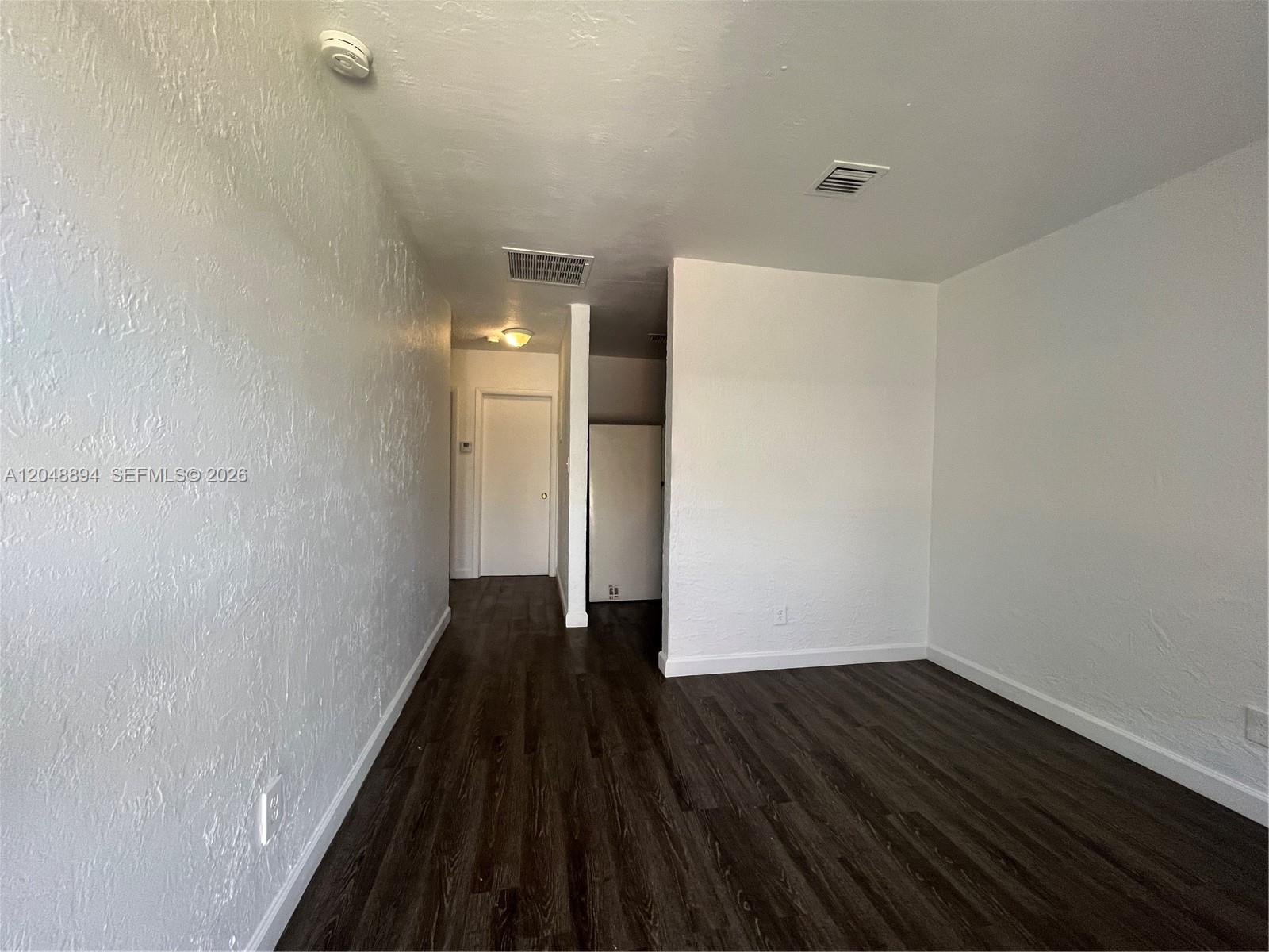An interior view shows a room with white walls, dark wood flooring, and a hallway — 3024 NW 2nd St, Pompano Beach FL 33069, POMPANO BEACH, FL