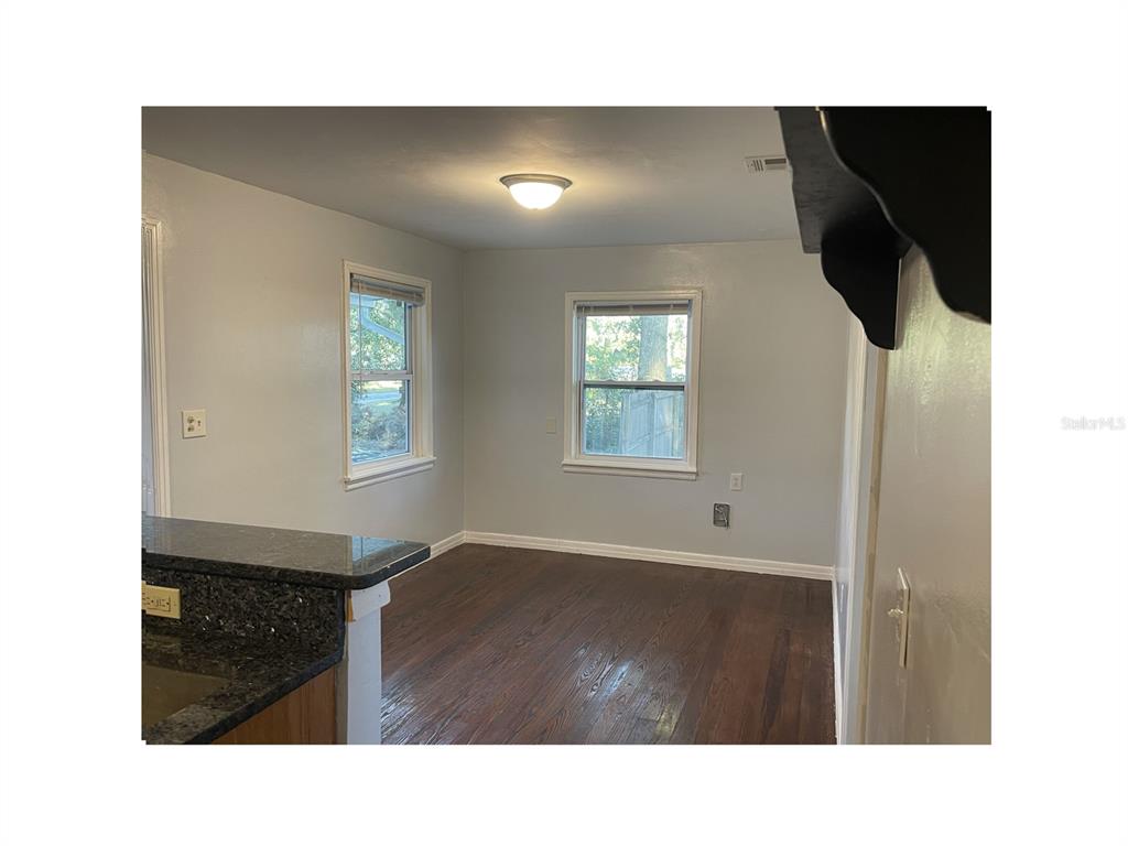 A kitchen with wood cabinets, dark countertops, and hardwood floors opens into a dining area — 6220 SE 118TH PLACE, BELLEVIEW, FL