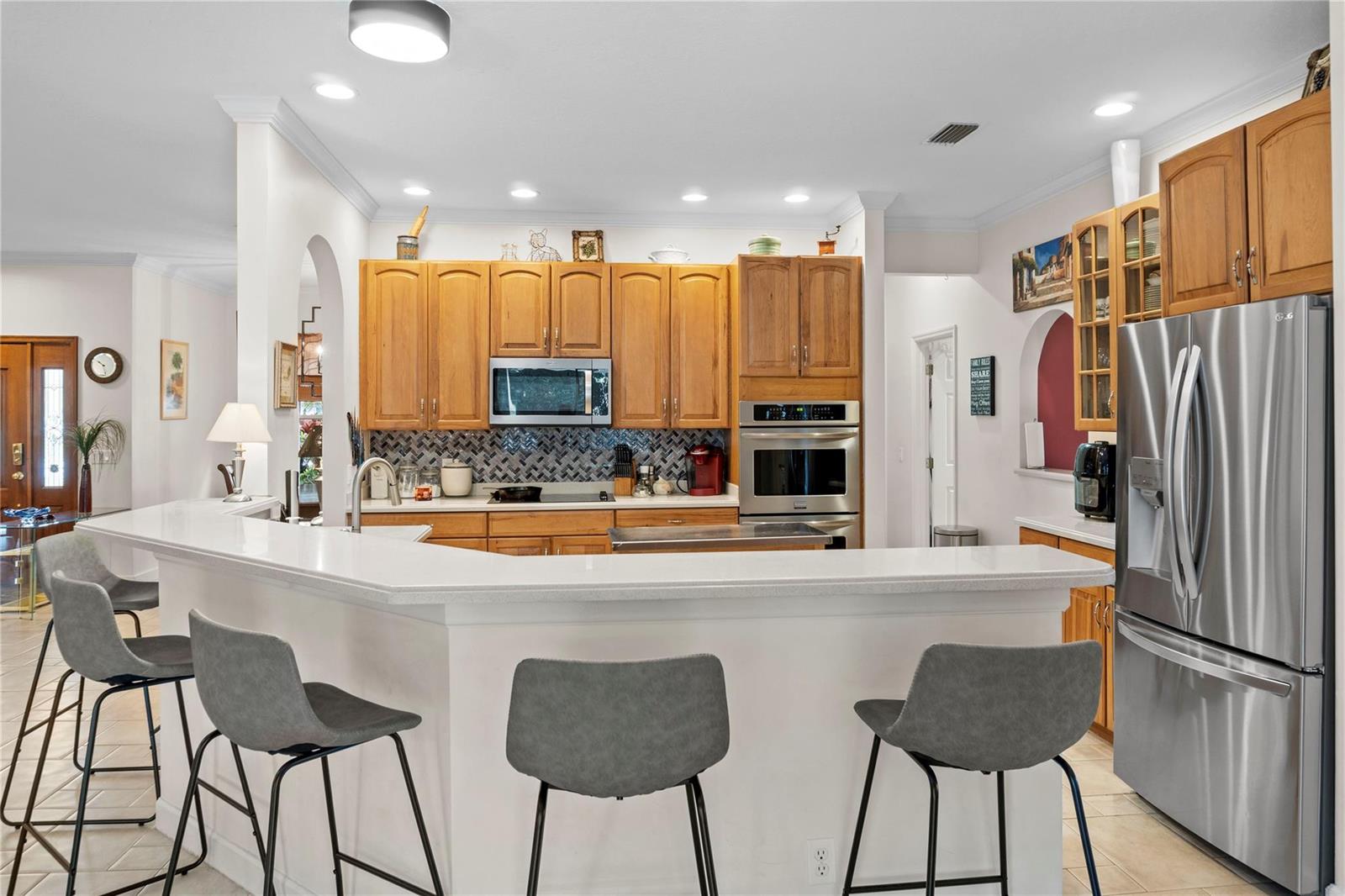 A kitchen with wood cabinets, stainless steel appliances, a white countertop, and three bar stools — 2148 Buena Vista Boulevard, Vero Beach FL 32960, VERO BEACH, FL