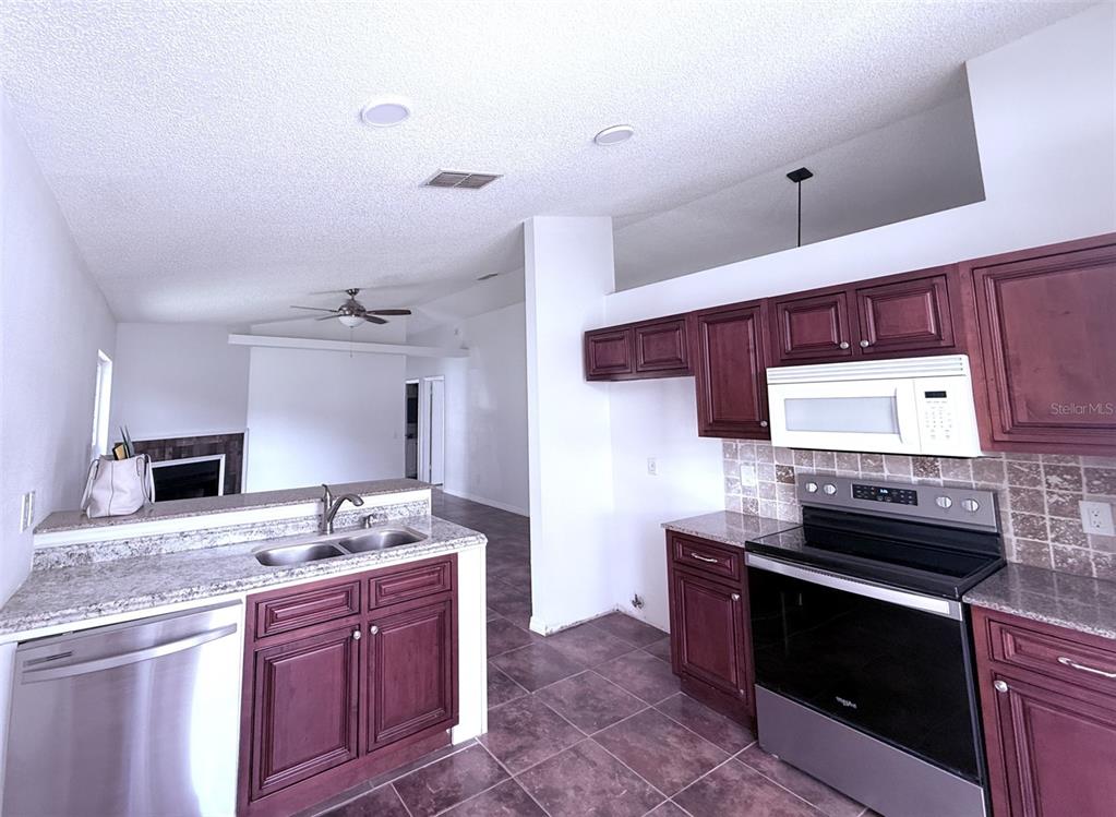 A kitchen with dark wood cabinets, granite countertops, and stainless steel appliances overlooks a living area — 7219 EDGEWATER SHORES COURT, ORLANDO, FL