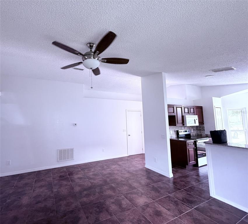 An open-concept living area features dark tile flooring, a ceiling fan, and an adjacent kitchen — 7219 EDGEWATER SHORES COURT, ORLANDO, FL