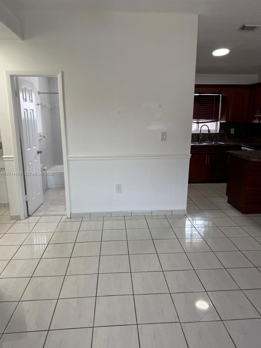A tiled room features a doorway leading to a bathroom and an adjacent kitchen area — 2212 W 74th St # 28, Hialeah FL 33016, HIALEAH, FL