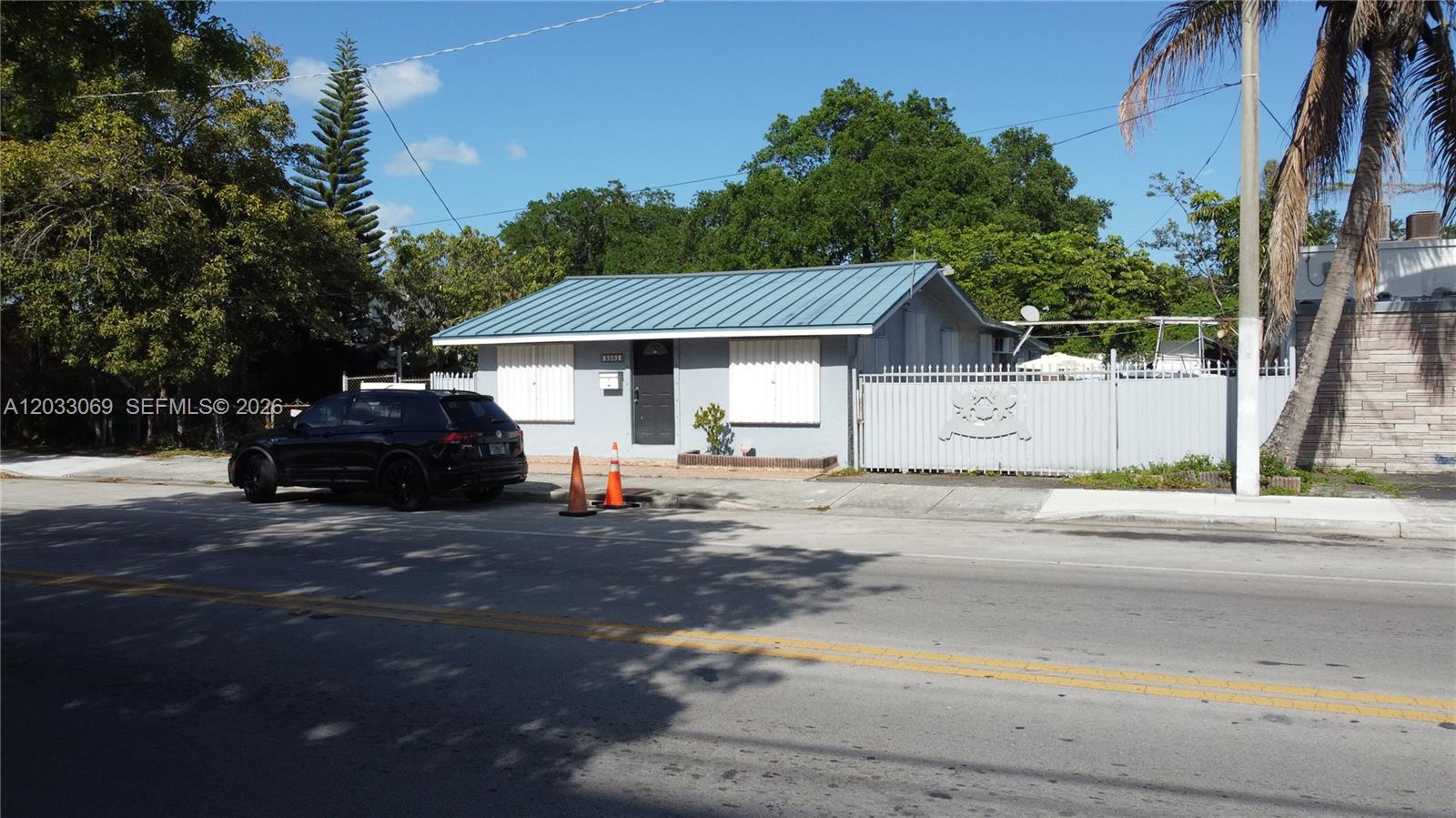 A single-story house with a blue metal roof sits behind a white metal fence — 5501 NW 2nd Ave, Miami FL 33127, MIAMI, FL
