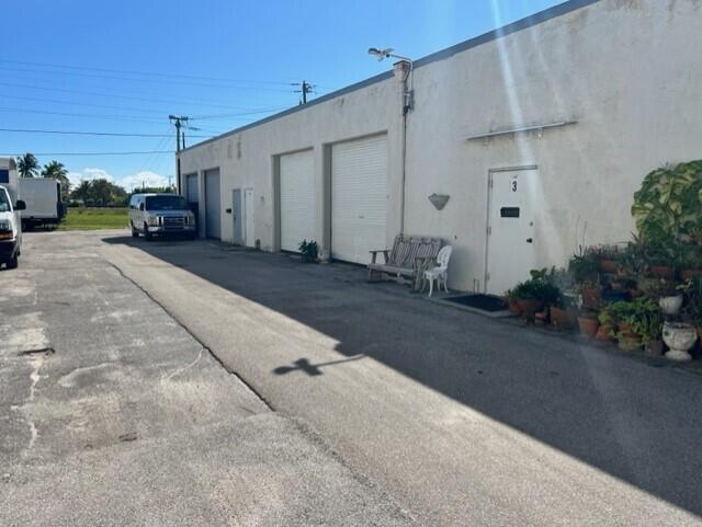 A white industrial building features multiple roll-up doors and a single entrance door with plants — 1460 S Cypress Drive # 9, Jupiter FL 33469, JUPITER, FL