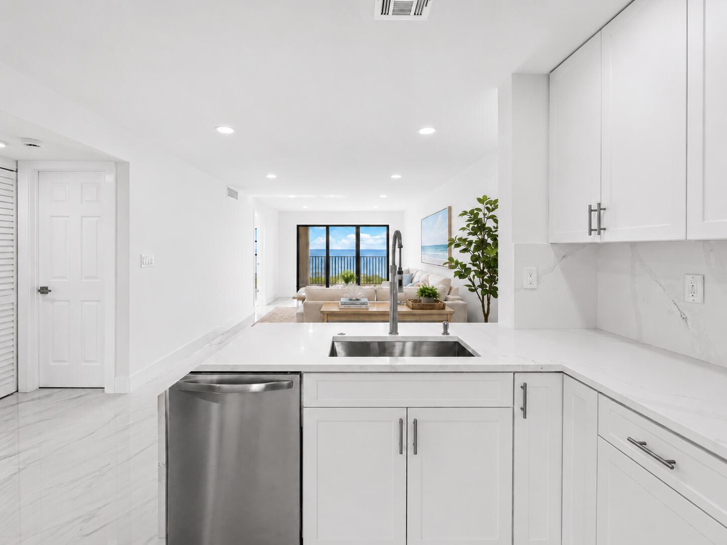 A white kitchen with marble countertops and stainless steel appliances overlooks a bright living area — 7420 S Ocean Drive # 314, Jensen Beach FL 34957, JENSEN BEACH, FL