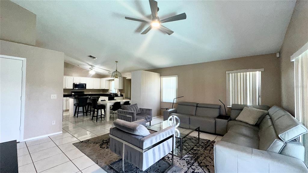 An open-concept living room features gray furniture, tile flooring, and an adjacent kitchen with white cabinets — 223 LAKE DAVENPORT ESTATES DRIVE, DAVENPORT, FL