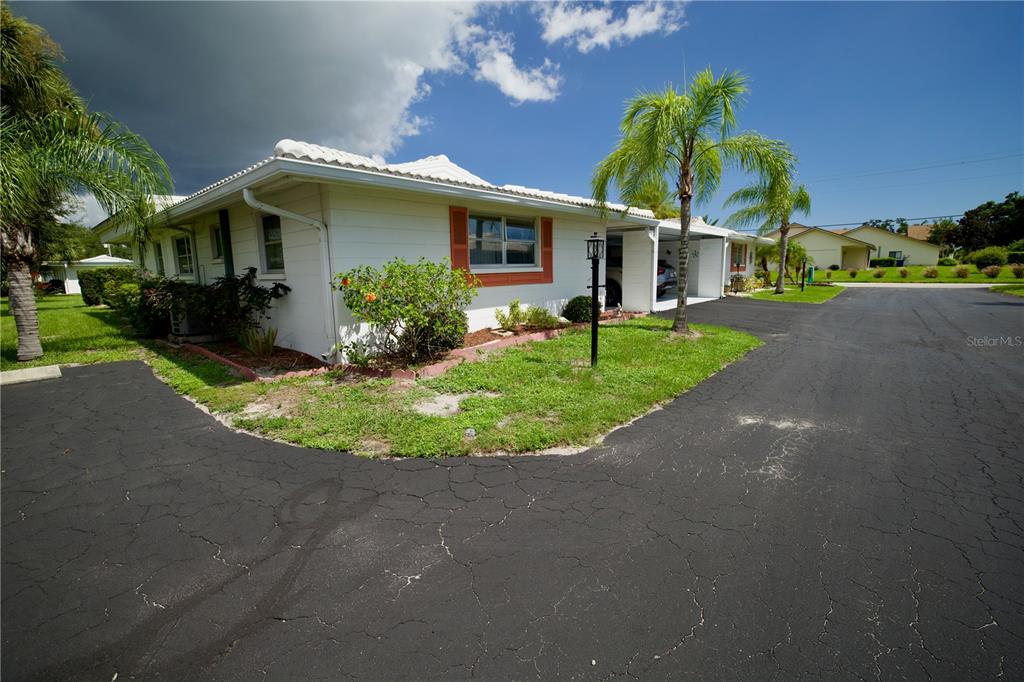 A white single-story house with orange shutters and a carport sits beside an asphalt driveway — 1741 CARIBBEAN CIRCLE UNIT 13, VENICE, FL