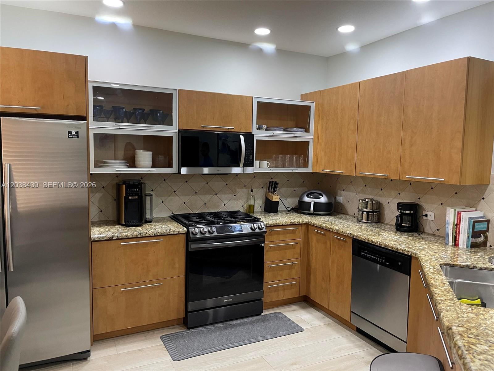 A kitchen features wood cabinets, stainless steel appliances, granite countertops, and a tile backsplash — 2900 NW 125th Ave # 107, Sunrise FL 33323, SUNRISE, FL