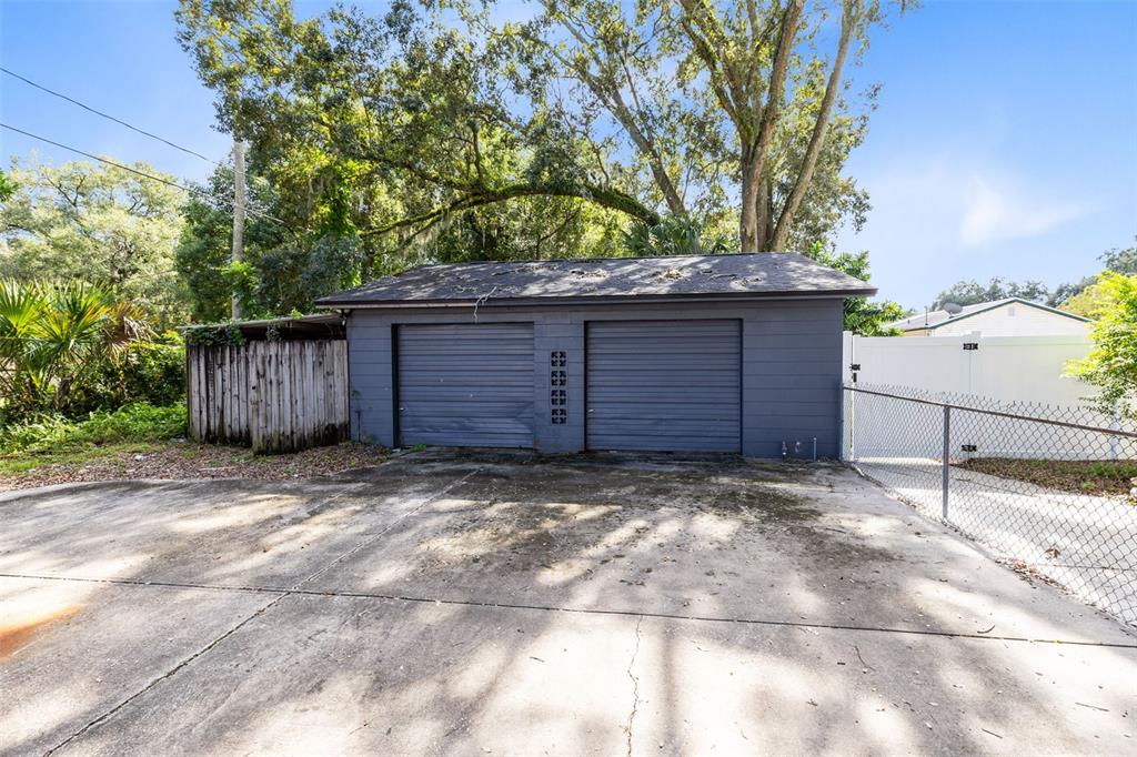 A detached two-car garage with gray siding and a concrete driveway sits under large trees — 701 E 25TH STREET, SANFORD, FL