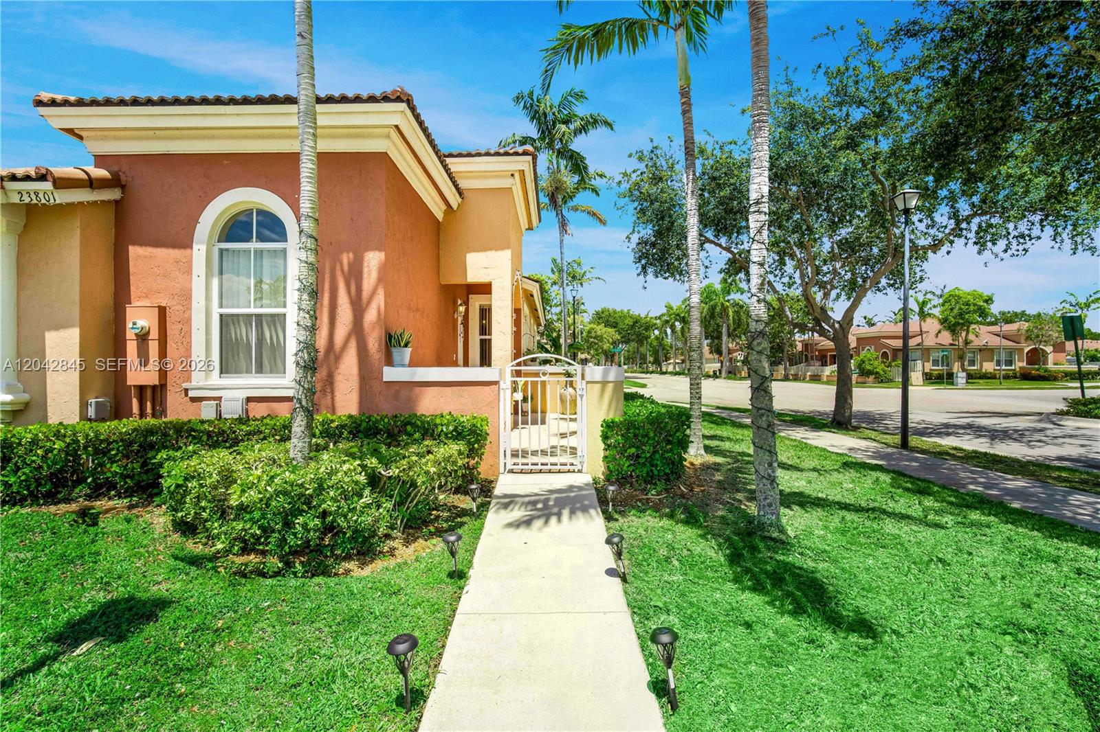 A sidewalk leads to the gated entrance of a stucco house with a arched window — 23801 SW 109th Pl, Homestead FL 33032, HOMESTEAD, FL