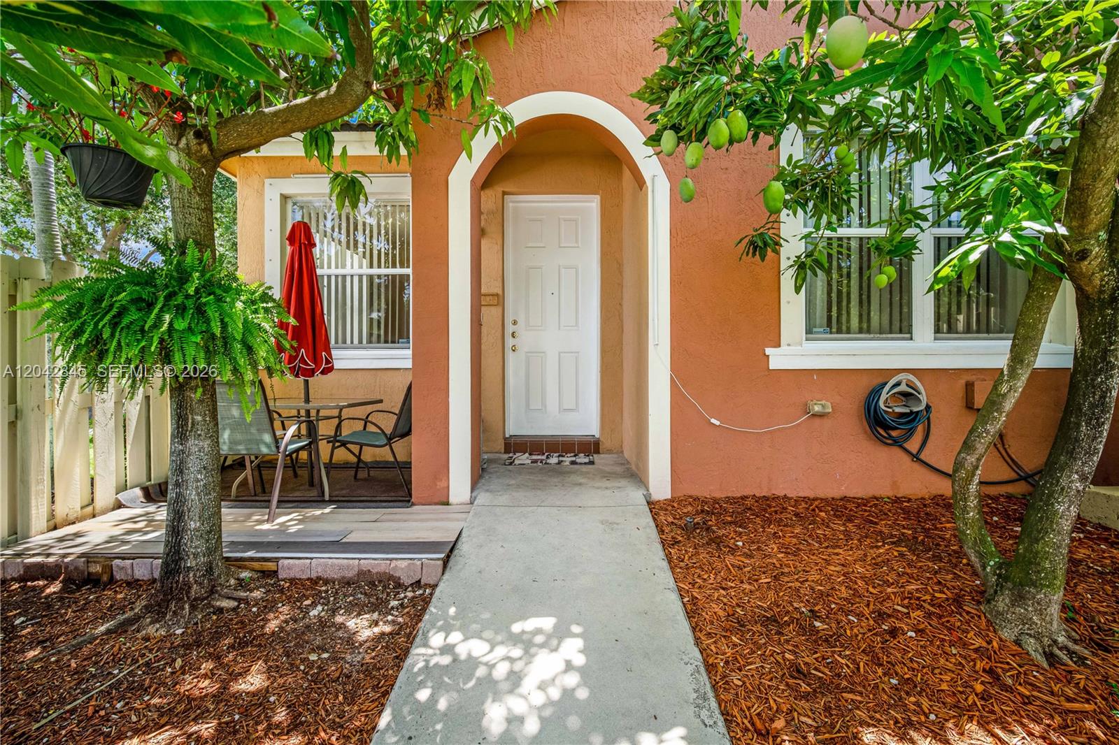 A concrete walkway leads to the white front door of a peach-colored house with landscaping — 23801 SW 109th Pl, Homestead FL 33032, HOMESTEAD, FL