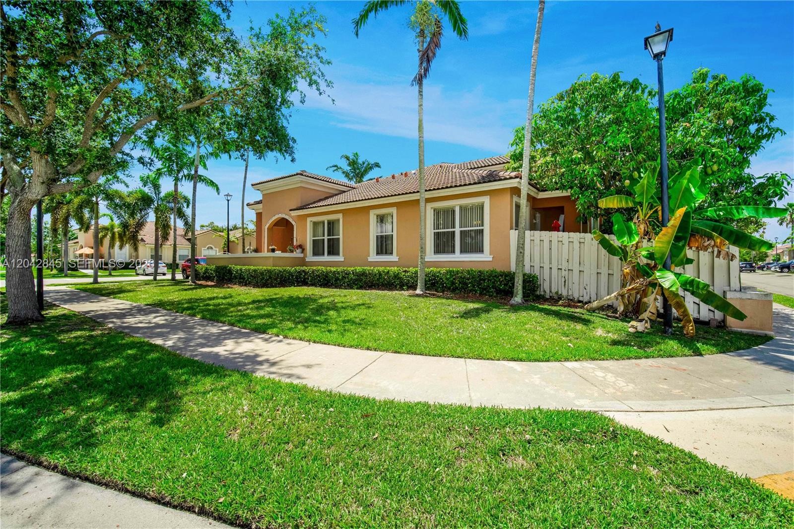 A single-story tan house with a tiled roof is surrounded by green lawn and palm trees — 23801 SW 109th Pl, Homestead FL 33032, HOMESTEAD, FL