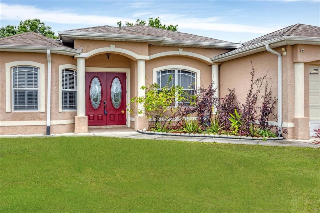The exterior of a tan stucco house features a red double front door and columns — 12108 HERNANDO ROAD, NORTH PORT, FL