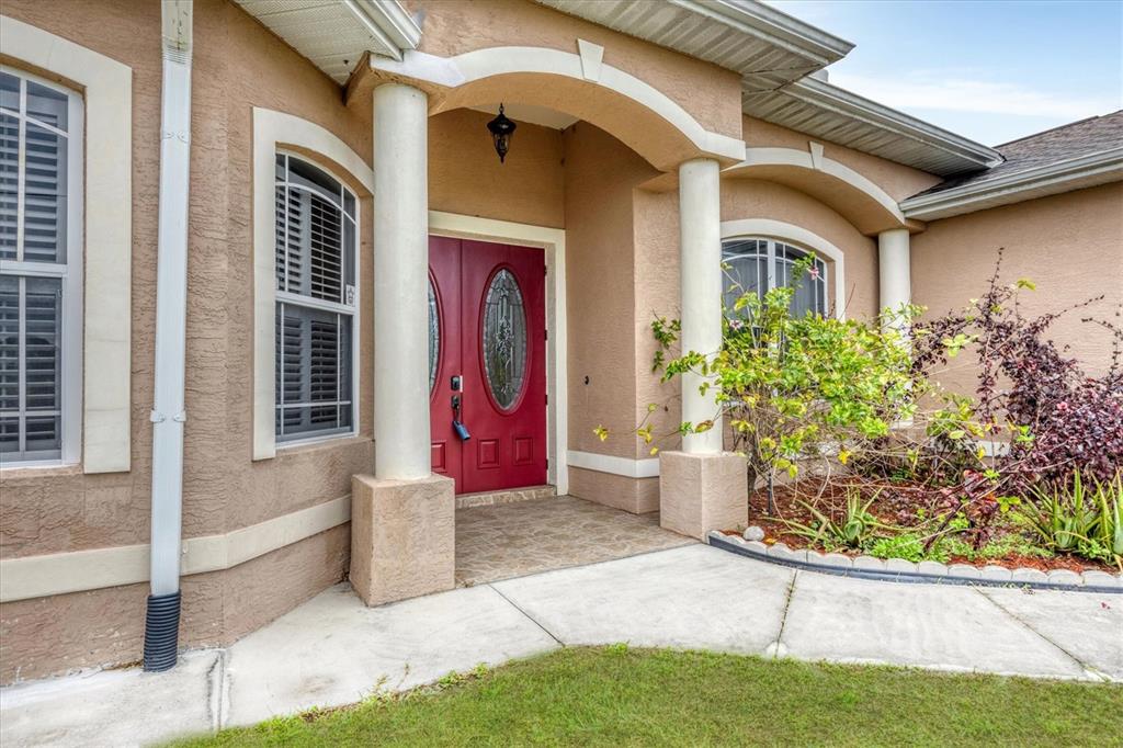 The exterior of a tan stucco house features a red double front door and columns — 12108 HERNANDO ROAD, NORTH PORT, FL