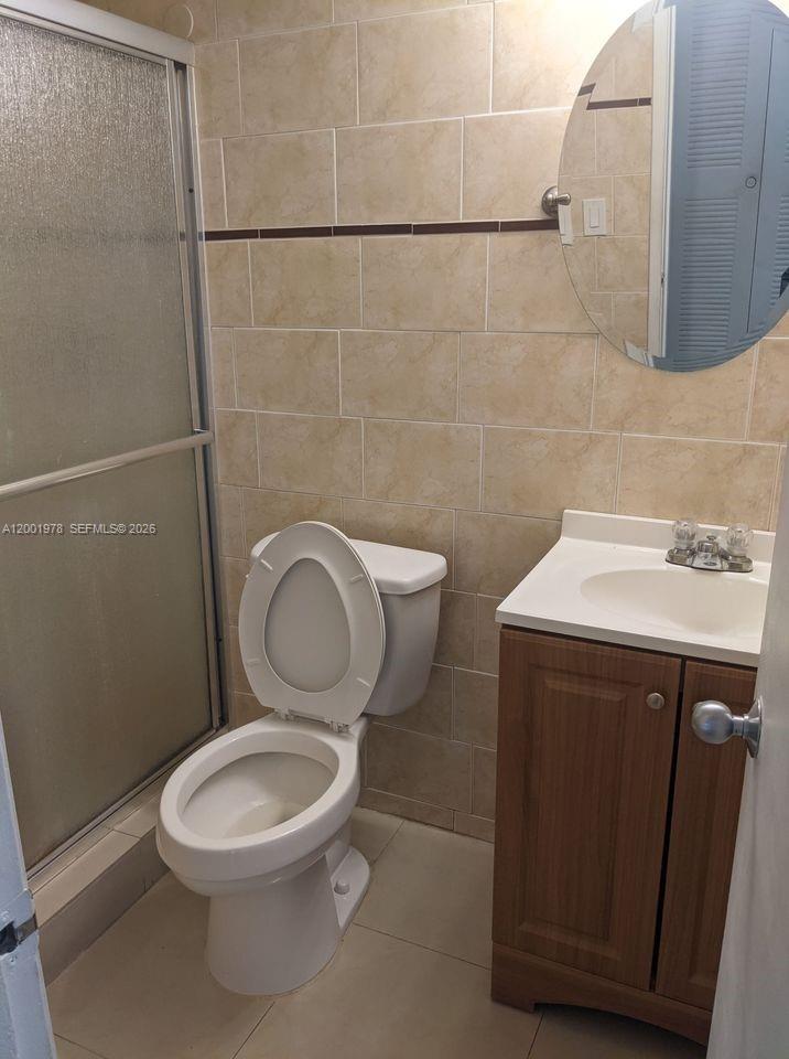 A small bathroom features a glass shower stall, a white toilet, and a wood vanity — 7125 NW 186th St # B209, Hialeah FL 33015, HIALEAH, FL