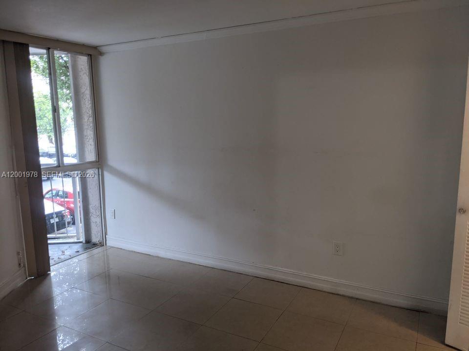 An empty room with light-colored tile flooring and a sliding glass door leading outside — 7125 NW 186th St # B209, Hialeah FL 33015, HIALEAH, FL