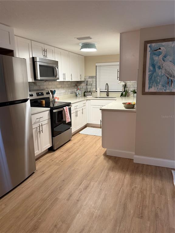 A kitchen features white cabinets, stainless steel appliances, light countertops, and wood-look flooring — 2849 MARLETTE STREET, SARASOTA, FL