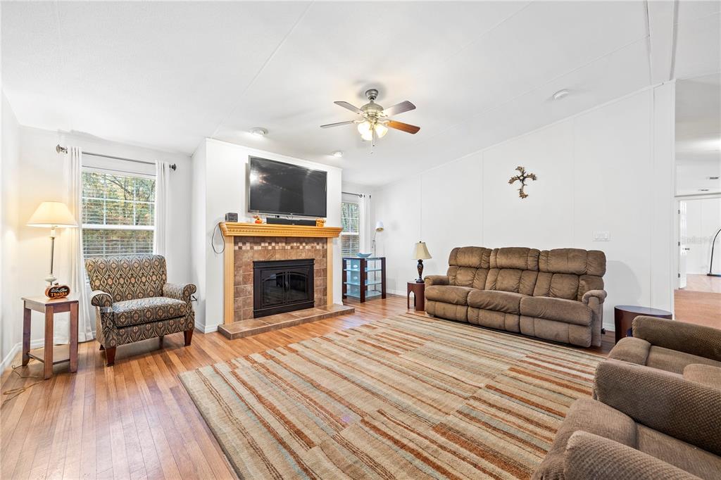 A living room features a fireplace, a ceiling fan, wood flooring, and brown furniture — 1366 SW CENTRAL TERRACE, FORT WHITE, FL