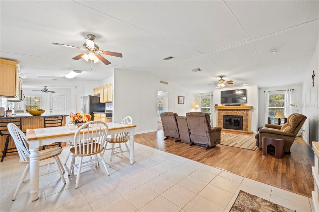 An open-concept living and dining area features tile flooring, wood-look laminate, and a stone fireplace — 1366 SW CENTRAL TERRACE, FORT WHITE, FL