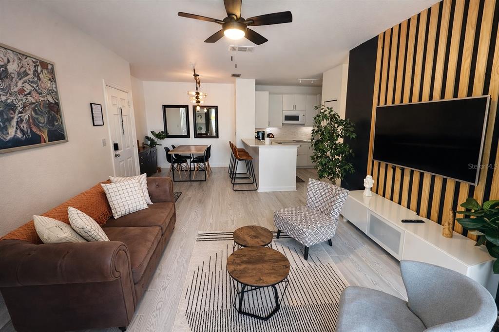 A living room with a brown sofa, patterned armchair, wood-slat accent wall, and open kitchen — 8824 DUNES COURT COURT UNIT 103, KISSIMMEE, FL